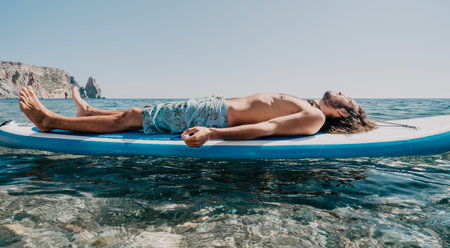man sup yoga. Happy sporty man practising yoga pilates on paddle sup surfboard. male stretching...