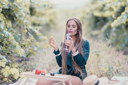 Woman picnic vineyard. Happy woman with a glass of wine at a picnic in the vineyard, wine tasting at sunset and open nature in the summer. Romantic dinner, fruit and wine.の写真素材