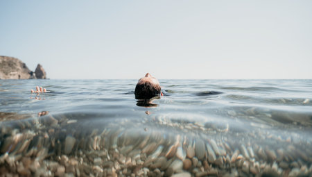Woman swimming in sea at sunset, float on calm water back view. Concept of body image and fitness, enjoying a serene beach. Happy woman with perfect fit body enjoys sea beachの写真素材