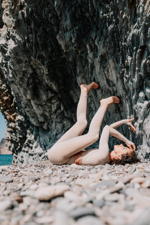 Woman travel sea. Sporty happy middle aged posing on a beach near the sea on background of volcanic rocks, like in Iceland, sharing travel adventure journeyの写真素材