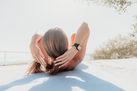 Fitness woman sea. Happy middle aged woman in orange sportswear exercises morning outdoors on yoga...