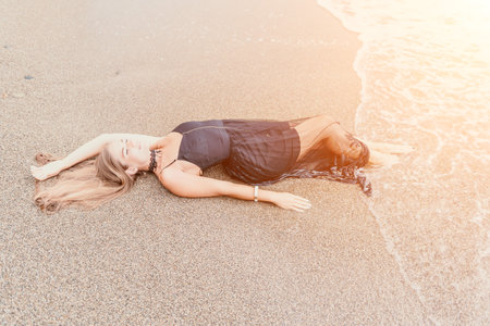 Woman summer travel sea. Happy tourist in black dress enjoy taking picture outdoors for memories. Woman traveler posing on sea beach surrounded by volcanic mountains, sharing travel adventure journeyの写真素材
