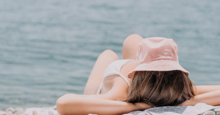 Unrecognizable positive woman in white bikini sunbathing or tanning on seaside beach during summer. happy tourist enjoying sun tan lying on beach chair lounge at luxury resortの写真素材