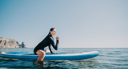 Woman sup yoga. Happy sporty woman practising yoga pilates on paddle sup surfboard. Female stretching doing workout on sea water. Modern individual female hipster outdoor summer sport activity.の写真素材