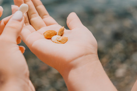 Woman eating milky almond nuts. A young caucasian woman chopping fresh green almond after morning fitness yoga near sea. Only hands are visibly. Healthy vegan food. Slow motion. Close upの写真素材