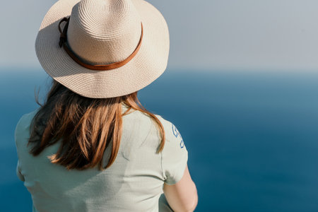 Woman travel sea. Happy tourist in hat enjoy taking picture outdoors for memories. Woman traveler posing on the beach at sea surrounded by volcanic mountains, sharing travel adventure journeyの写真素材