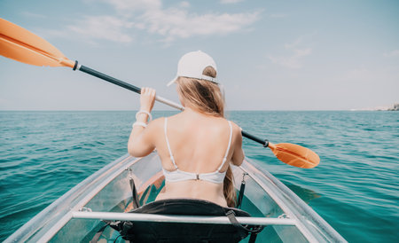 Woman in kayak back view. Happy young woman with long hair floating in transparent kayak on the...