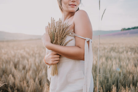 A woman is holding a bunch of wheat in her arms. The wheat is dry and brown, and the woman is wearing a white dress. The scene is set in a field, and the woman is posing for a photoの写真素材