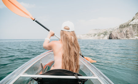 Woman in kayak back view. Happy young woman with long hair floating in transparent kayak on the...