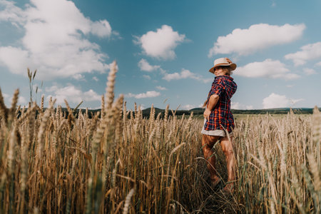 Woman farmer walks through a wheat field at sunset, touching green ears of wheat with his hands. Hand farmer is touching ears of wheat on field in sun, inspecting her harvest. Agricultural business.の写真素材