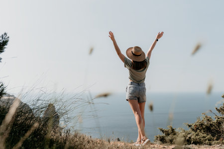 Woman travel sea. Happy tourist in hat enjoy taking picture outdoors for memories. Woman traveler posing on the beach at sea surrounded by volcanic mountains, sharing travel adventure journeyの写真素材