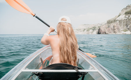 Woman in kayak back view. Happy young woman with long hair floating in transparent kayak on the...