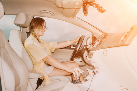 A woman in a yellow shirt is driving a car. She is wearing glasses and has her hands on the steering...