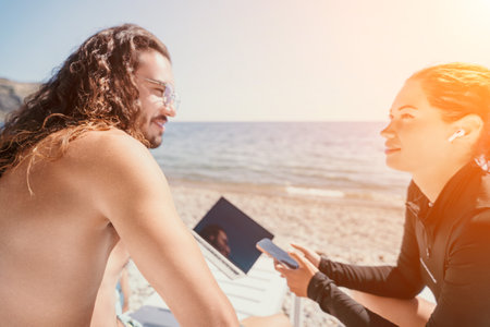 Man woman laptop sea. Working remotely on seashore. Happy successful couple, freelancers working on sea beach, relieves stress from work to restore life balance. Freelance, remote work on vacationの写真素材