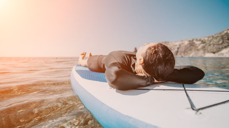 Woman sup yoga. Happy sporty woman practising yoga pilates on paddle sup surfboard. Female stretching doing workout on sea water. Modern individual female hipster outdoor summer sport activity.の写真素材