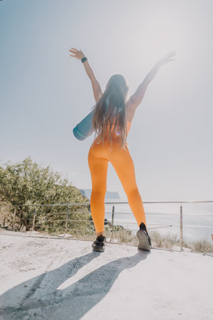 Fitness woman sea. Happy middle aged woman in orange sportswear exercises morning outdoors on yoga...