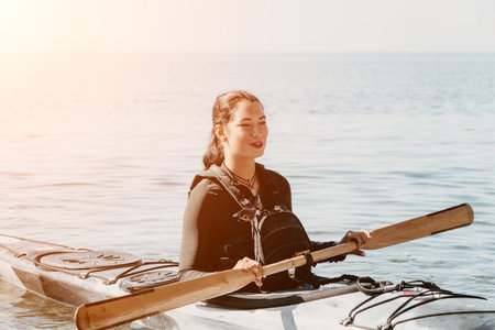 Woman sea kayak. Happy smiling woman in kayak on ocean, paddling with wooden oar. Calm sea water and horizon in background. Active lifestyle at sea. Summer vacation.の写真素材