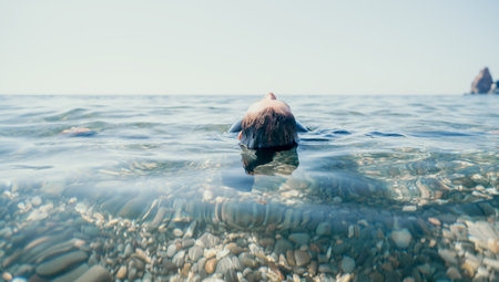 Woman swimming in sea at sunset, float on calm water back view. Concept of body image and fitness, enjoying a serene beach. Happy woman with perfect fit body enjoys sea beachの写真素材