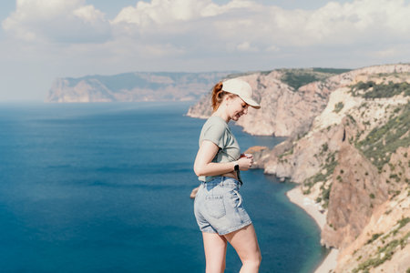 Woman travel sea. Happy tourist in hat enjoy taking picture outdoors for memories. Woman traveler posing on the beach at sea surrounded by volcanic mountains, sharing travel adventure journeyの写真素材