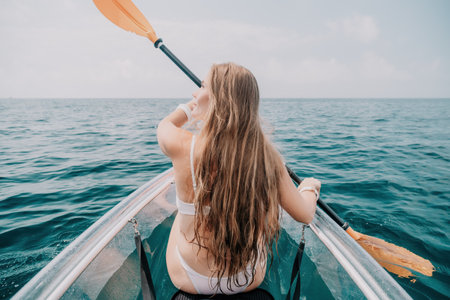 Woman in kayak back view. Happy young woman with long hair floating in transparent kayak on the...