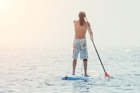 Man Sup Sea. Strong athletic man learns to paddle sup standing on board in open sea ocean on sunny...