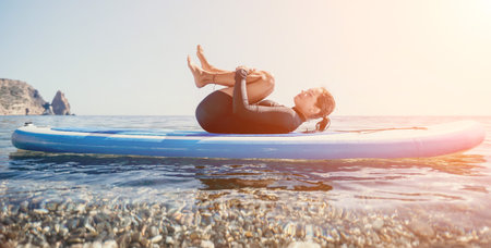 Woman sup yoga. Happy sporty woman practising yoga pilates on paddle sup surfboard. Female...