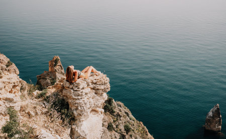 Woman travel sea. Happy tourist enjoy taking picture outdoors for memories. Woman traveler looks at the edge of the cliff on the sea bay of mountains, sharing travel adventure journeyの写真素材