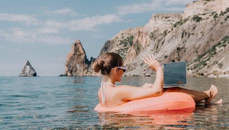 Woman freelancer works on laptop swimming in sea on pink inflatable ring. Happy tourist in...