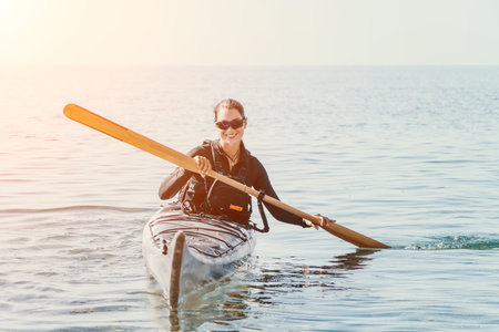 Woman sea kayak. Happy smiling woman in kayak on ocean, paddling with wooden oar. Calm sea water and horizon in background. Active lifestyle at sea. Summer vacation.の写真素材