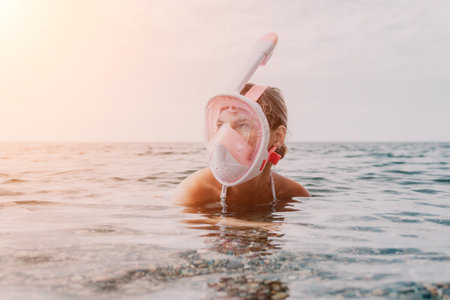 Young happy woman in white bikini and wearing pink mask gets ready for sea snorkeling. Positive smiling woman relaxing and enjoying water activities with family summer travel holidays vacation on sea.の写真素材