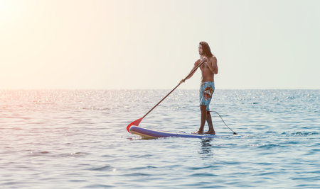 Man Sup Sea. Strong athletic man learns to paddle sup standing on board in open sea ocean on sunny...
