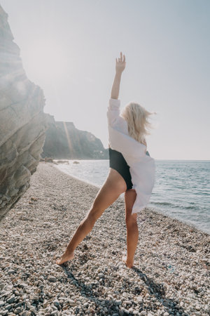 A Woman in a White Shirt and Black Swimsuit Poses on a Stony Beachの写真素材