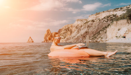 Woman freelancer works on laptop swimming in sea on pink inflatable ring. Happy tourist in...