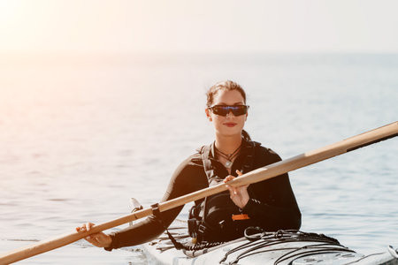 Woman sea kayak. Happy smiling woman in kayak on ocean, paddling with wooden oar. Calm sea water and horizon in background. Active lifestyle at sea. Summer vacation.の写真素材