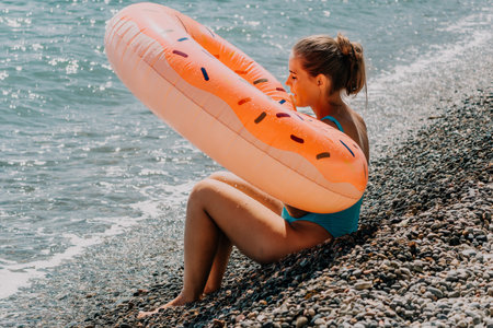 Young Woman Sitting on a Pebble Beach with a Donut Float