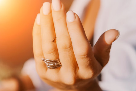 Ant walking by woman hand with a ring with feathers on her fingerの写真素材