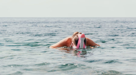 Young happy woman in white bikini and wearing pink mask gets ready for sea snorkeling. Positive smiling woman relaxing and enjoying water activities with family summer travel holidays vacation on sea.の写真素材