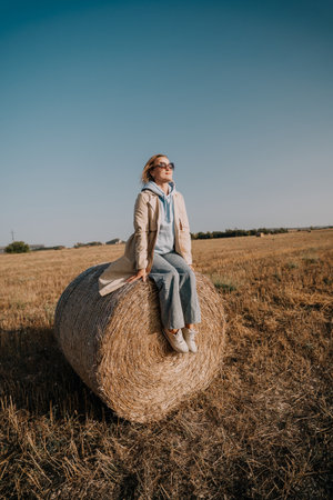 Woman in Sunglasses Sitting on a Hay Bale in a Fieldの写真素材