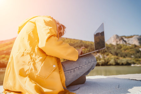 Laptop, Nature, Work - Woman in Yellow Raincoat Uses Laptop Outdoors Near Riverの写真素材