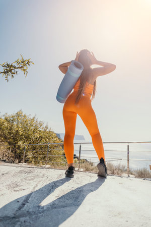 Woman in Orange Yoga Outfit with Mat on Backの写真素材