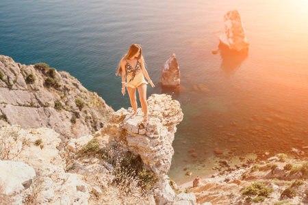 Woman travel sea. Happy tourist enjoy taking picture outdoors for memories. Woman traveler looks at the edge of the cliff on the sea bay of mountains, sharing travel adventure journeyの写真素材