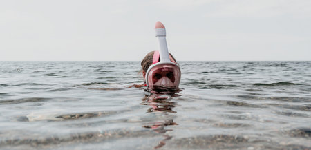 Young happy woman in white bikini and wearing pink mask gets ready for sea snorkeling. Positive smiling woman relaxing and enjoying water activities with family summer travel holidays vacation on sea.の写真素材