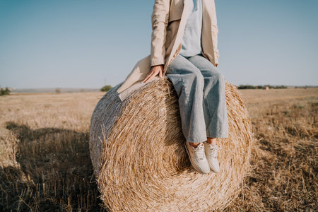 Woman in a Trench Coat Sitting on a Hay Bale in a Field