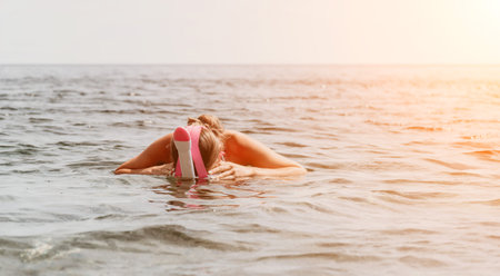 Young happy woman in white bikini and wearing pink mask gets ready for sea snorkeling. Positive smiling woman relaxing and enjoying water activities with family summer travel holidays vacation on sea.の写真素材
