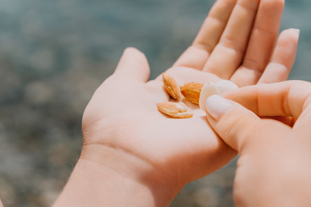 Woman eating almond nuts. A young caucasian woman chopping fresh green almond after morning fitness yoga near sea. Only hands are visibly. Healthy vegan food. Slow motion. Close upの写真素材