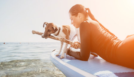 Sea woman sup. Silhouette of happy positive young woman with her dog, surfing on SUP board through calm water surface. Idyllic sunset. Active lifestyle at sea or river. Summer vacation with pets.の写真素材