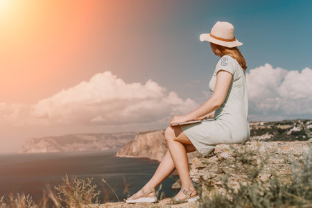 Woman Relaxing on Cliffside with Laptop and Ocean Viewの写真素材