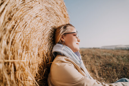 Woman Leaning Against Hay Bale, Autumn Fieldの写真素材