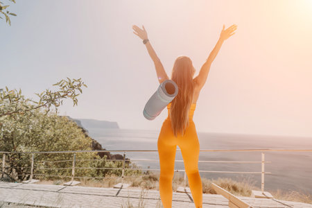 Woman in Yellow Outfit with Arms Raised, Standing on a Cliffsideの写真素材