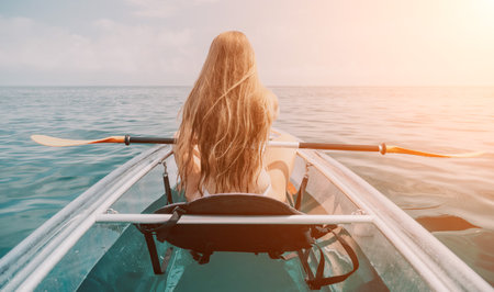Woman in kayak back view. Happy young woman with long hair floating in transparent kayak on the crystal clear sea. Summer holiday vacation and cheerful female people relaxing having fun on the boatの写真素材
